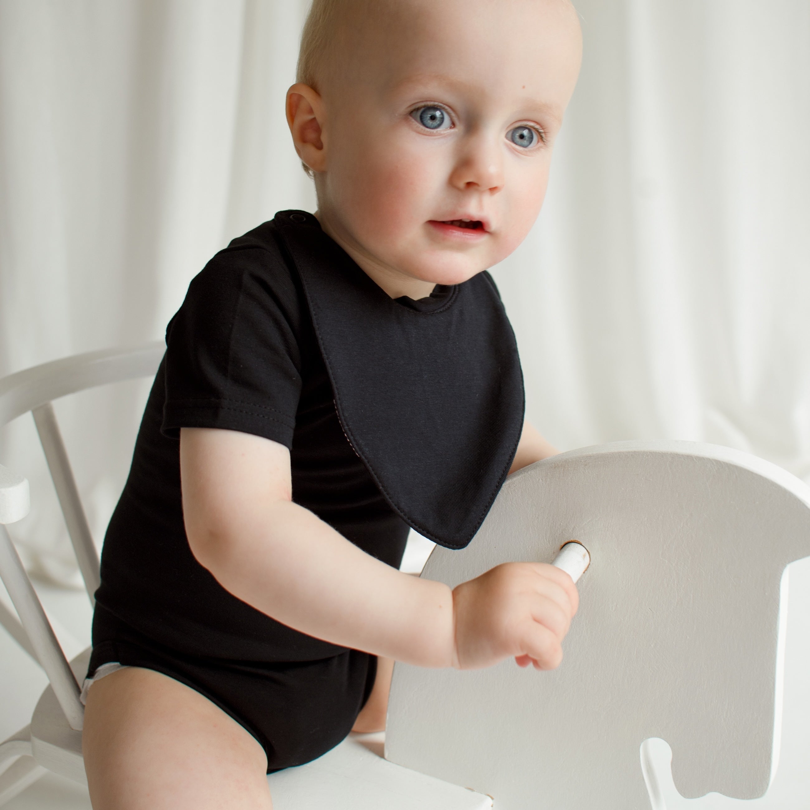 Little boy playing with a rocking horse, wearing a black CUUTTI short sleeve bodysuit and a matching black CUUTTI waterproof bib.